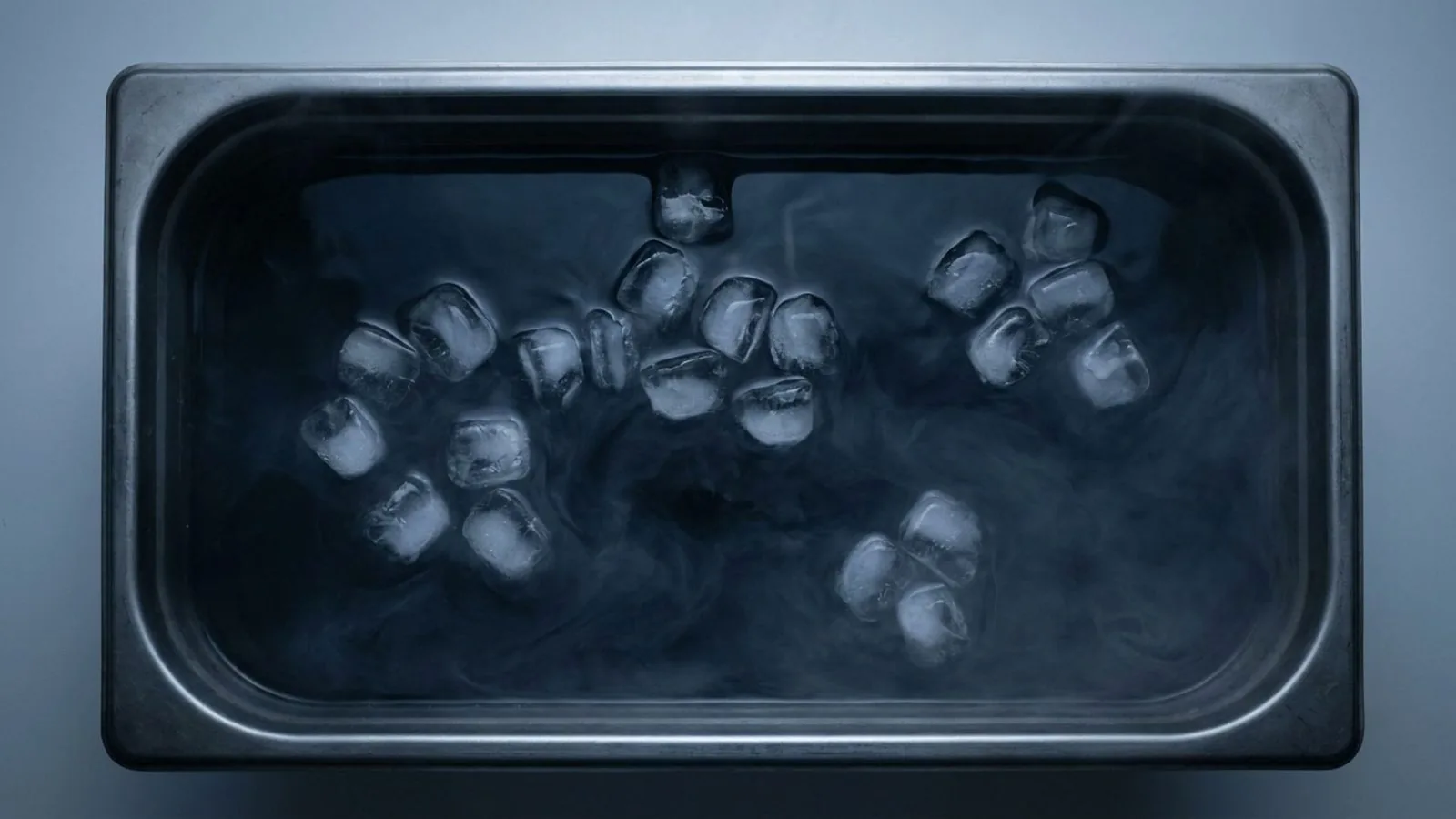 Looking straight down into dark still cold water with scattered melting ice cubes and thin surface mist